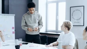 Kanban vs. Scrum: Ein Team arbeitet an einem Scrum-Projekt. Links steht ein Board mit der Aufschrift "Sprint 1" und Klebezetteln. Auf dem Tisch liegen ein Tablet und Scheibutensilien.