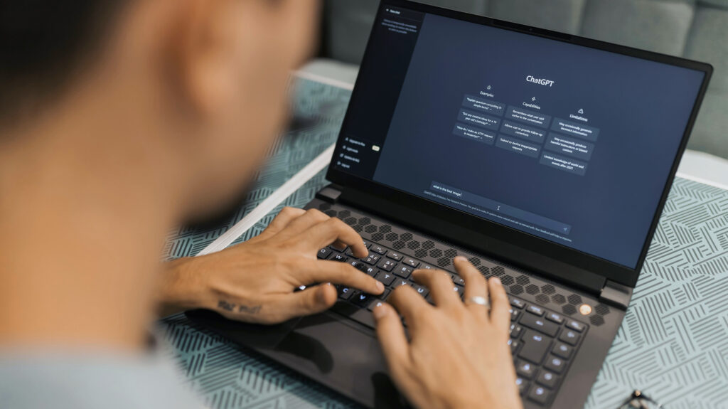 Ein Mann sitzt an einem Tisch vor seinem Laptop und hat ChatGPT geöffnet.
